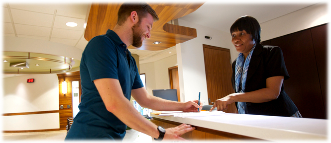 A man fills out a document at the front desk of the tribunal. The staff person behind the desk smiles and gives him instructions.