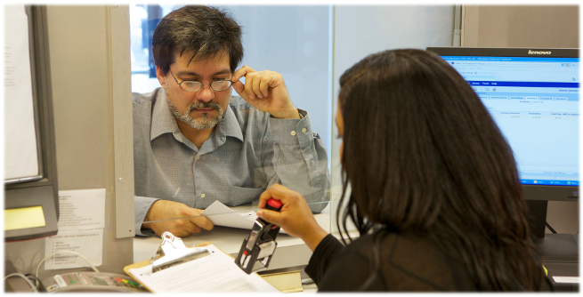 A man adjusts he glass as he watches a woman date stamp his forms.