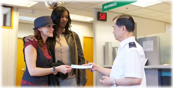 Two women show their notice of hearing to a commissionaire.