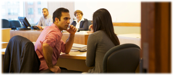 Au premier plan une femme et son avocat, assis à un bureau, consultent pendant l'audience.