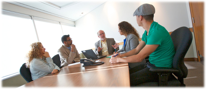 A male mediator or adjudicator explains something to four people sitting at a boardroom table.